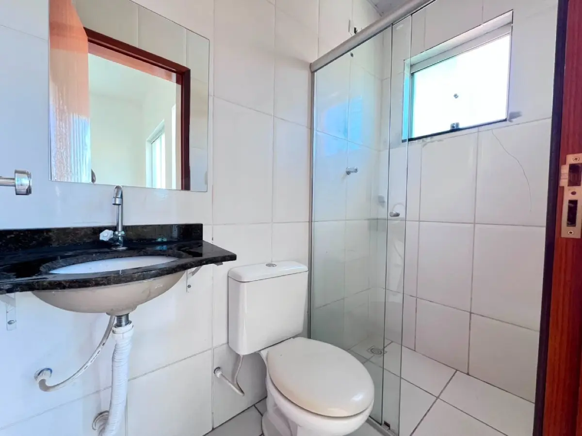 Banheiro com box em vidro, bancada preta e revestimento branco